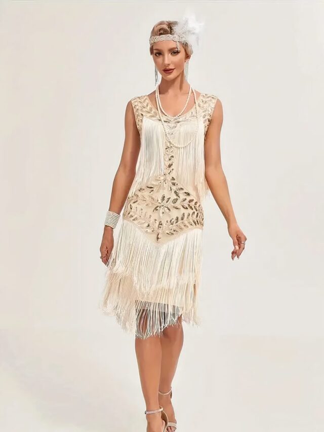 Photo d'une femme portant une robe beige style années 20 sans manches à franges en haut et en bas et paillettes, encolure ronde avec un serre-tête élastique argenté orné de plumes blanches et un bracelet en perles blanche multi rangs, le tout sur un fond beige clair