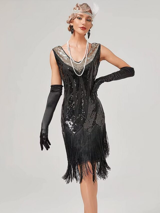 Photo d'une jeune femme portant une robe année 20 noire style Gatsby art déco à paillettes et franges, de longs gants en satin noir et un serre-tête à plumes, le tout sur un fond gris