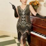 Photo d'une femme debout devant un piano droit ouvert et portant une robe vintage années 20 noire et dorée mi-longue à col V avec des longs gants noirs et un serre-tête argenté , dans une pièce aux murs beige et sol beige et gris à motifs géométriques