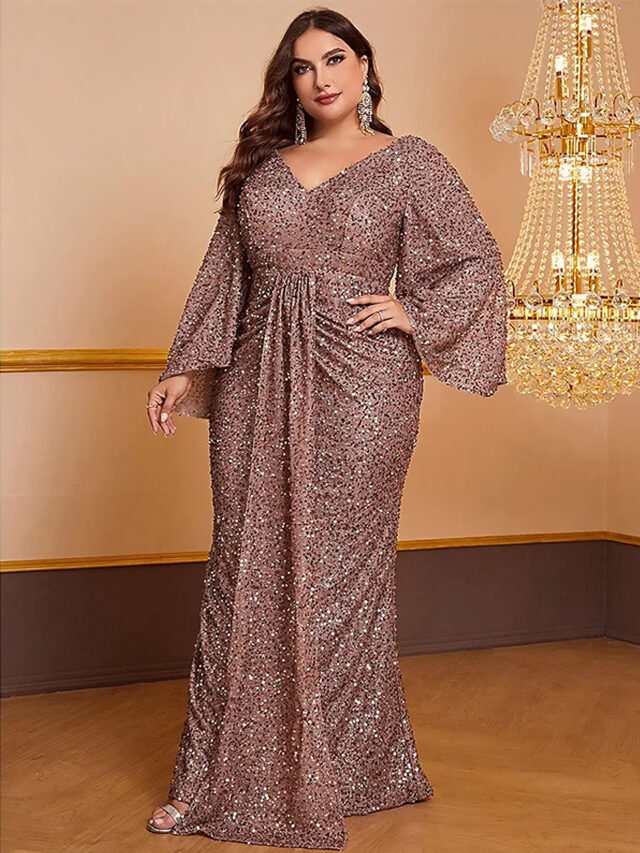 Photo d'une femme forte portant une robe de soirée à paillettes rose poudrée, devant un mur aux tons orangees avec un lustres en cristal en arriere plan