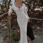 femme brune sur un sentier de plage qui porte une robe en mailles ajourées blanche très longue.