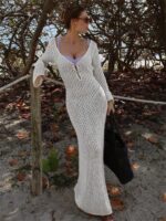 femme brune sur un sentier de plage qui porte une robe en mailles ajourées blanche très longue.
