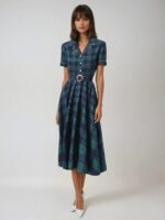 Photo d'une robe années 50 mi-longue automne-hiver à carreaux dominance bleu marine portée par une jeune femme brune sur un fond gris