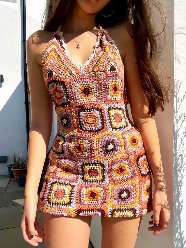 Photo d'une jeune femme debout devant un mur portant une mini robe années 70 au crochet style patchwork à dominance orange