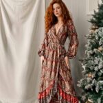 Photo d'une femme portant une robe portefeuille bohème à motifs manches longues devant un rideau blanc à côté d'un sapin.