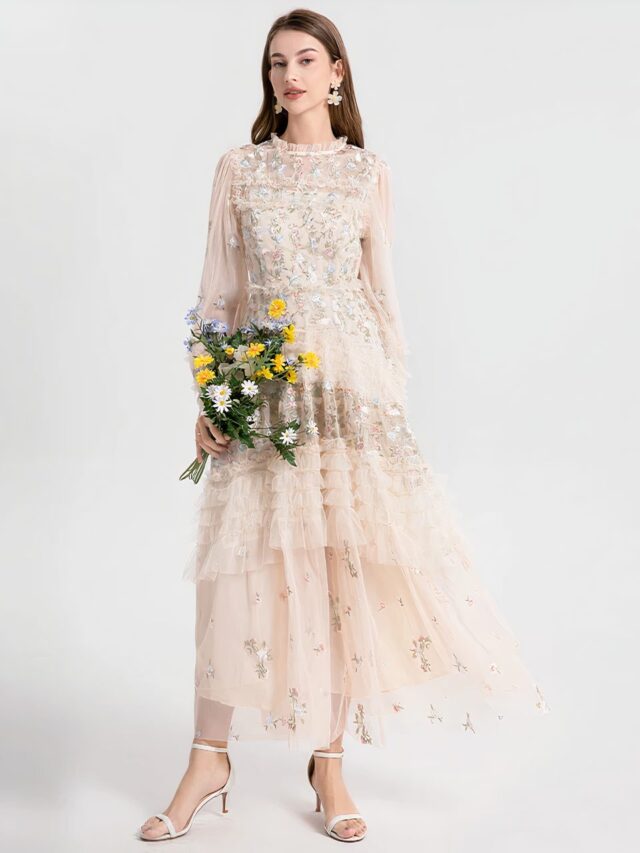 Femme portant une robe bohème chic beige en mousseline brodée de fleurs avec un bouquet de fleurs dans les mains.