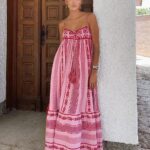 Photo d'une femme portant une robe bohème rose longue bi-matière, se tenant contre un mur blanc, devant une porte en bas,