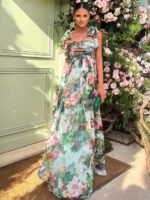 Photo d'une femme portant une robe ne mousseline fleurie devant des fleurs et une porte verte.