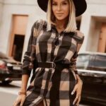 On voit une femme qui porte une robe chemise à carreaux beige, marron et noire.