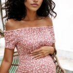 Une femme enceinte brune porte une robe rose à fleurs blanches
