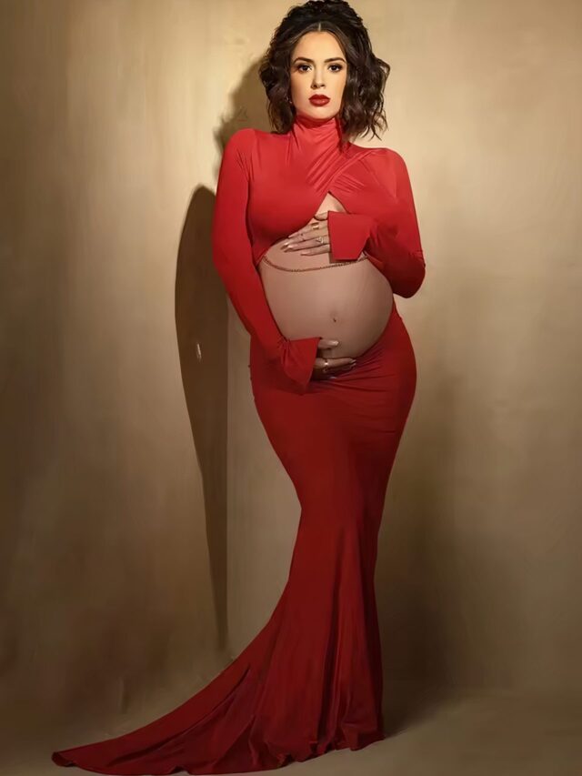 Une femme enceinte brune porte une robe longue rouge avec des manches longues. Il n'y a pas de tissu sur le ventre