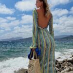 Photo d'une femme portant une robe dos nu longue bleu et jaune au crochet devant la mer