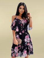 Photo d'une femme portant une robe fleurie noire et rose avec des bretelles et des manches courtes tombantes. elle porte un sac pochette dans une main et se touche les cheveux avec l'autre.