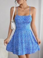 Photo d'une femme portant une robe fleurie bleue courte à bretelles avec un sac à main porté épaule blanc.