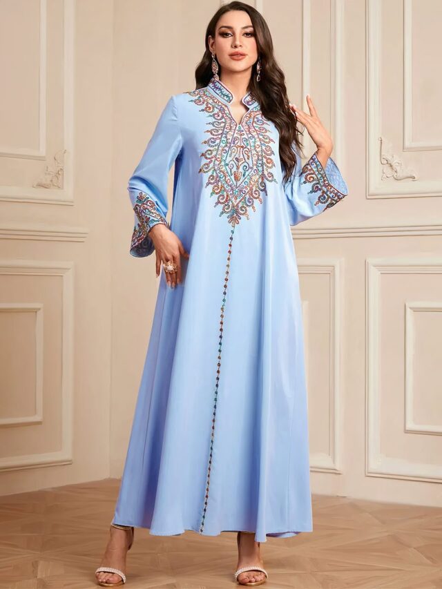 Photo d'une femme dands une pièce aux murs cossus portant une robe kabyle bleue de forme trapèze et broderies devant et au bord des manches