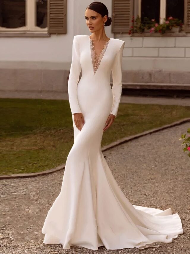 Photo d'une femme portant une robe mariage blanche à col V et épaulettes forme sirène à traîne dans un jardin