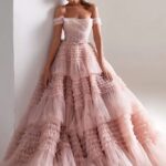Photo d'une femme portant une robe de princesse rose à volants, se tenant contre un mur