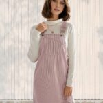Femme en robe salopette en velours côtelé rose poudré. Pull blanc