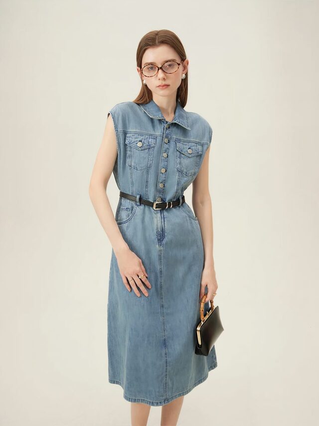 Photo d'une robe en jean vintage bleu sans manches portée par une femme brune à lunettes sur un fond beige