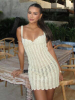Robe de plage sexy beige en macramé, portée par une femme qui s'appuye sur une table